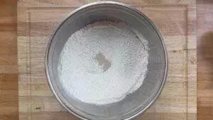 Stainless steel bowl with flour and yeast on a wooden board, ready for baking preparation.