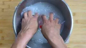 Hands mixing sticky rice in a metal bowl on a wooden surface.