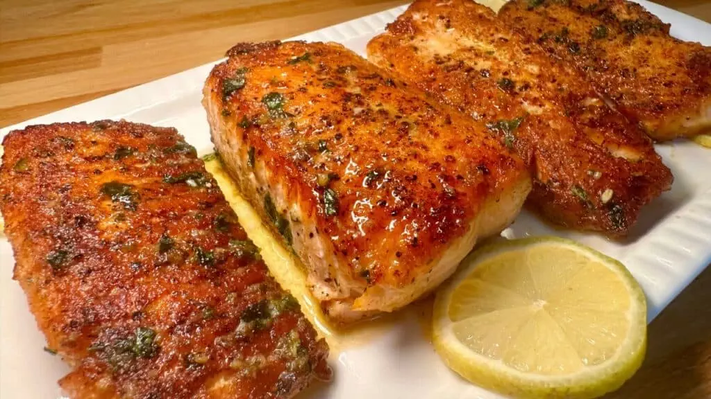 Grilled salmon fillets garnished with herbs and lemon slices on a white plate. Perfect for a healthy, flavorful meal.