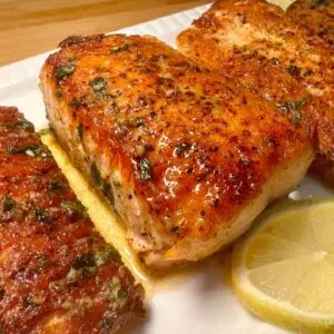 Grilled salmon fillets garnished with herbs and lemon slices on a white plate. Perfect for a healthy, flavorful meal.