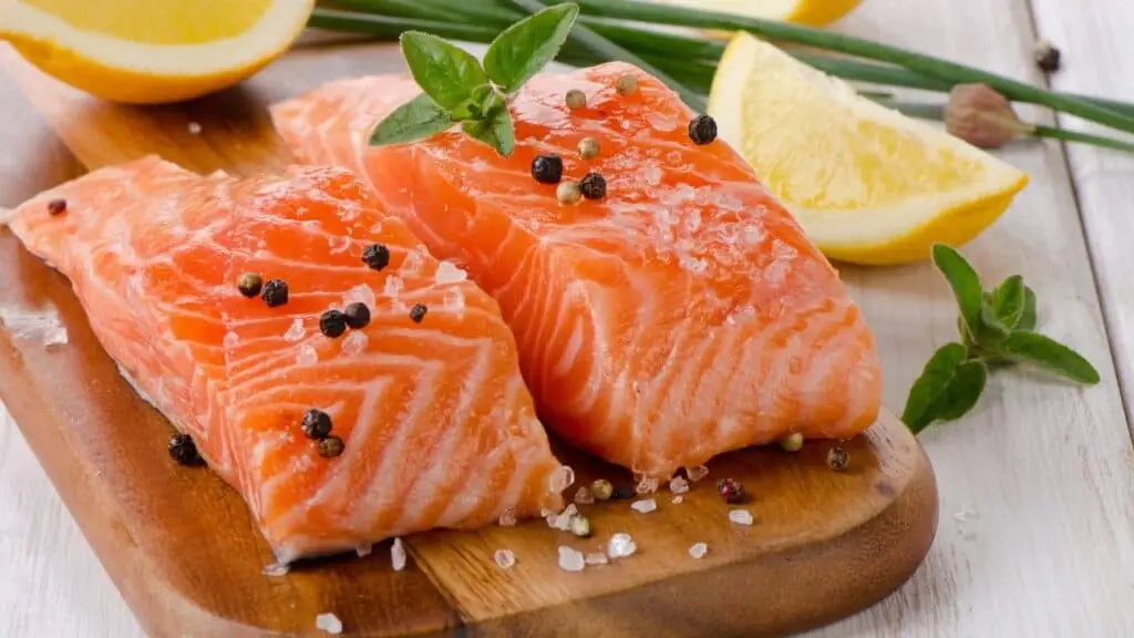 Fresh salmon fillets with peppercorns and lemon on a wooden board, ideal for healthy cooking and seafood recipes.