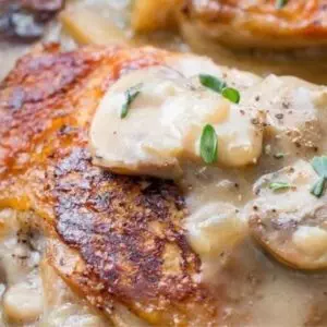 Creamy garlic mushroom chicken with crispy skin in sauce, garnished with herbs.