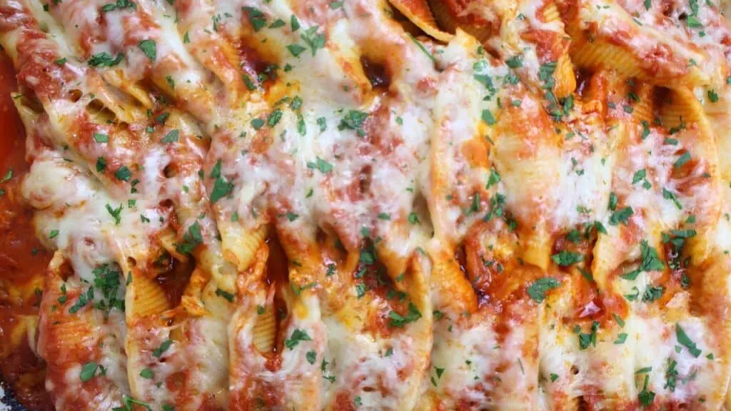 Baked pasta shells with melted cheese and fresh herbs in tomato sauce, close-up view. Perfect comfort food dish.