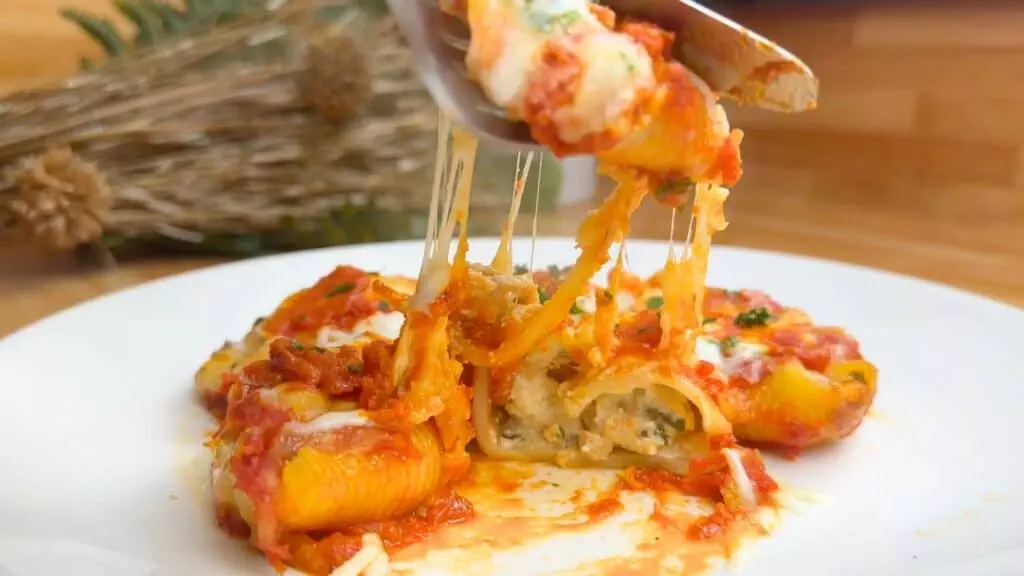 Cheesy stuffed pasta shells with tomato sauce and herbs, served on a white plate. Perfect Italian comfort food.