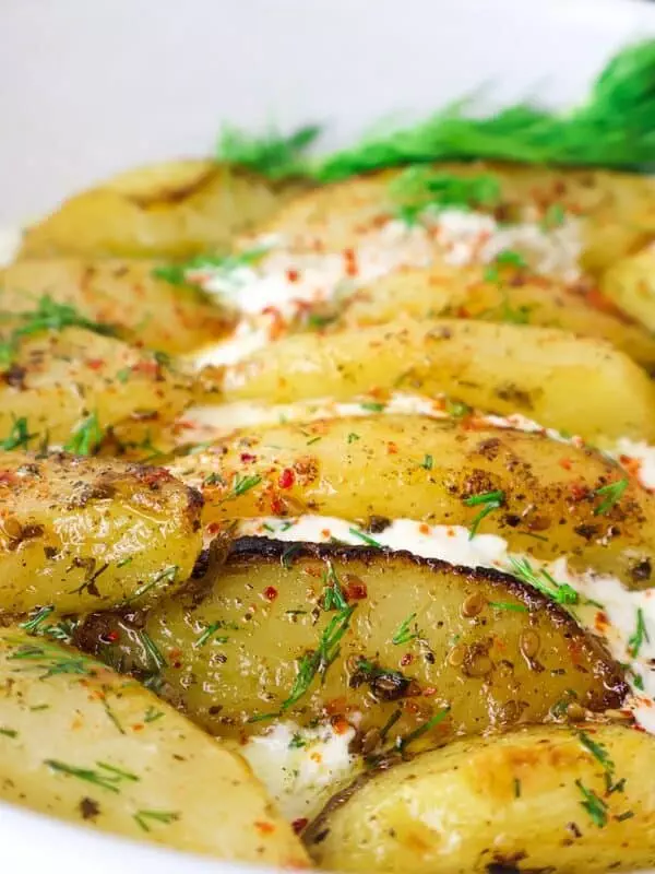 Delicious oven-roasted potatoes with herbs and spices, garnished with fresh dill in a white dish.