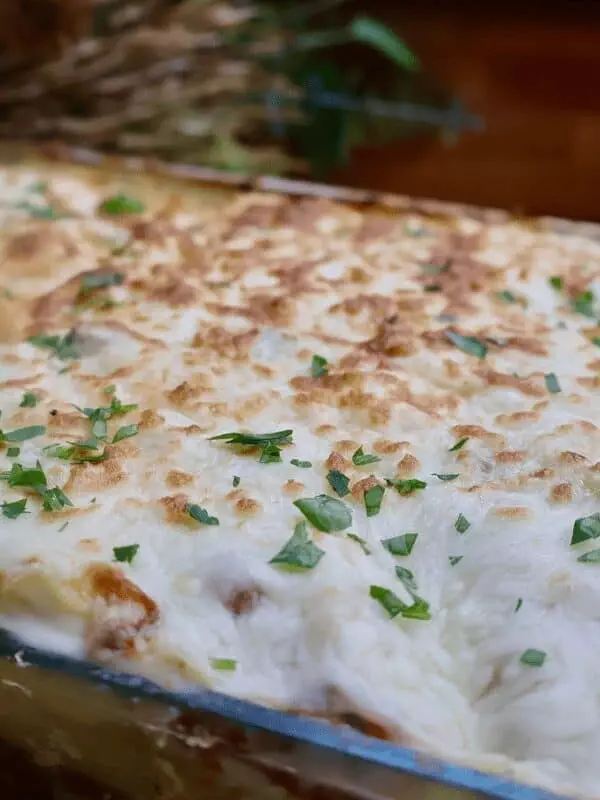 Delicious homemade baked lasagna topped with cheese and fresh herbs in a glass dish.