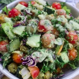 Fresh veggie salad with tomatoes, cucumbers, kale, and creamy dressing in a white bowl, perfect for a healthy meal.