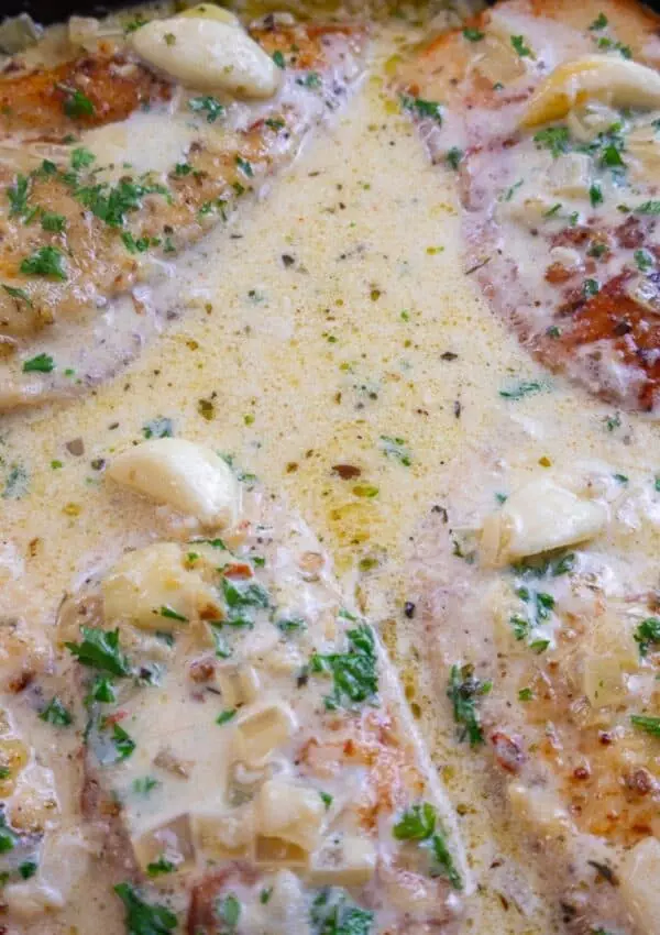 Creamy garlic chicken breasts with herbs in a skillet, perfectly cooked for a delicious meal.