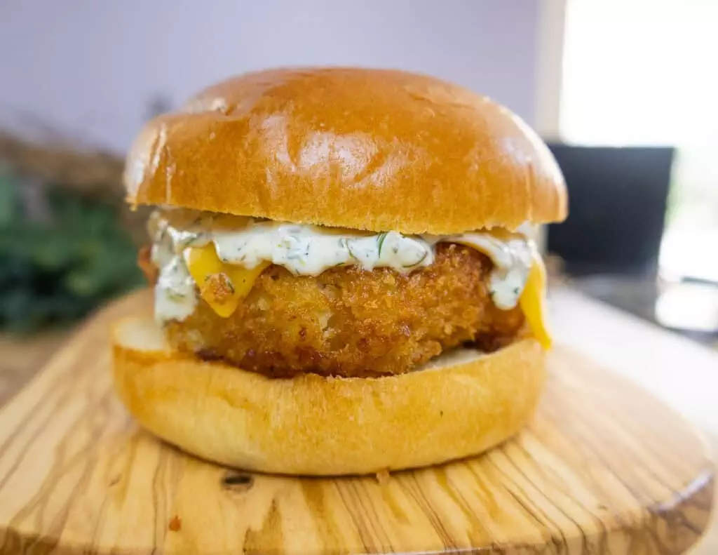 Close-up of a crispy chicken burger with cheese and sauce on a wooden board.