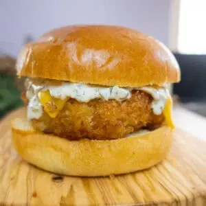 Close-up of a crispy chicken burger with cheese and sauce on a wooden board.