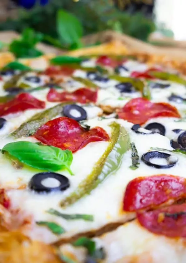 Close-up of a delicious pizza with pepperoni, olives, and fresh basil on a crispy crust.