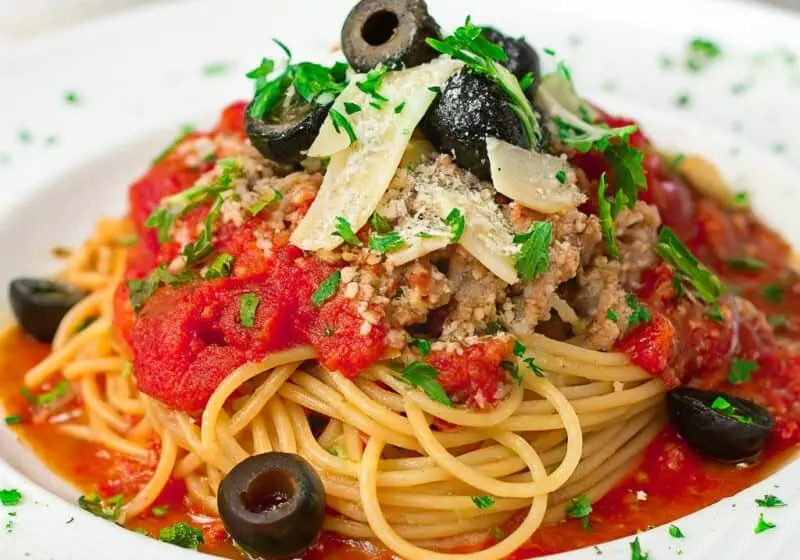 Delicious spaghetti with tomato sauce, ground meat, olives, and parmesan cheese, garnished with fresh parsley.