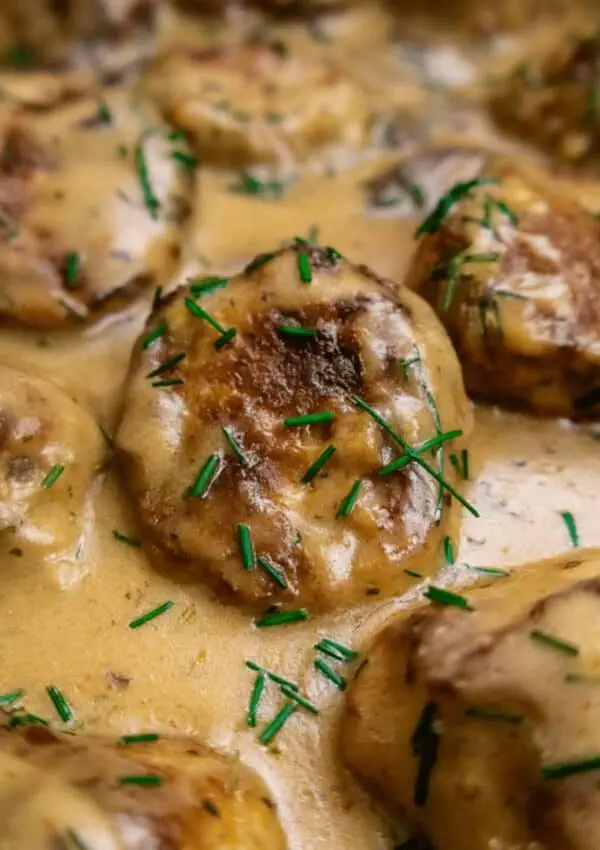 Creamy Swedish meatballs garnished with fresh chives in rich brown sauce, close-up.