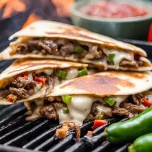 Grilled beef quesadillas with melted cheese, peppers, and jalapeños on a sizzling grill, served with salsa.