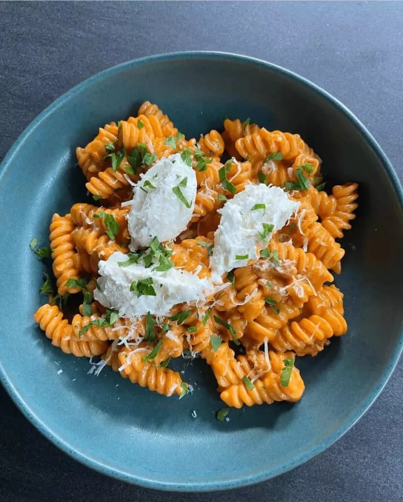 Creamy rotini pasta with ricotta, garnished with fresh herbs in a blue bowl on a dark surface.