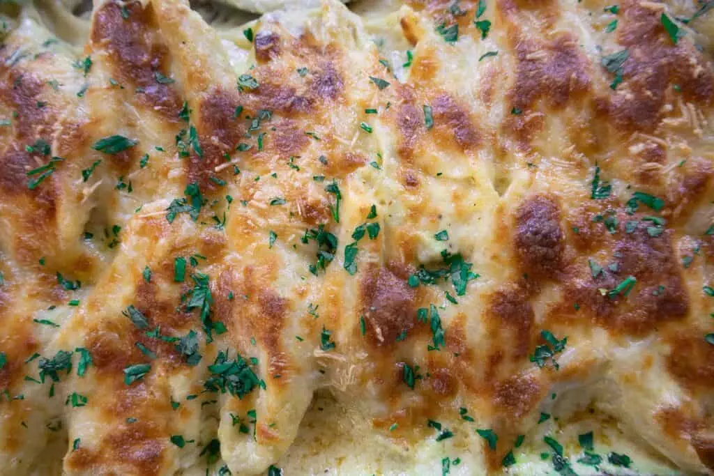 Close-up of golden baked cheesy pasta topped with fresh parsley, capturing its delicious texture and savory appeal.