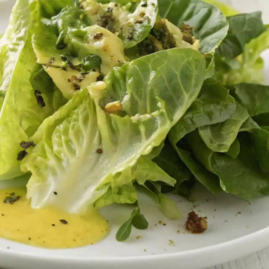 Fresh green salad with creamy dressing on a white plate, garnished with herbs and nuts, close-up shot.