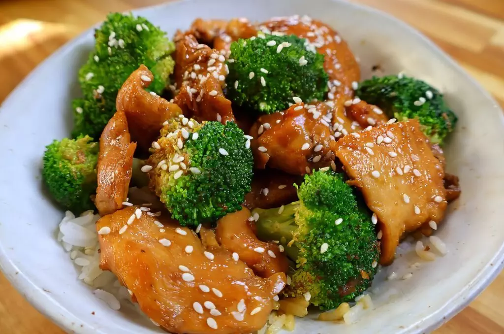 Stir-fried chicken and broccoli with sesame seeds over rice in a bowl. Healthy Asian-inspired dish.