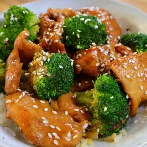 Stir-fried chicken and broccoli with sesame seeds over rice in a bowl. Healthy Asian-inspired dish.