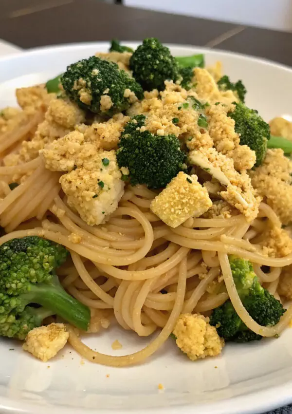 Tofu and broccoli pasta on a white plate, garnished with creamy sauce, perfect for a healthy vegan meal.