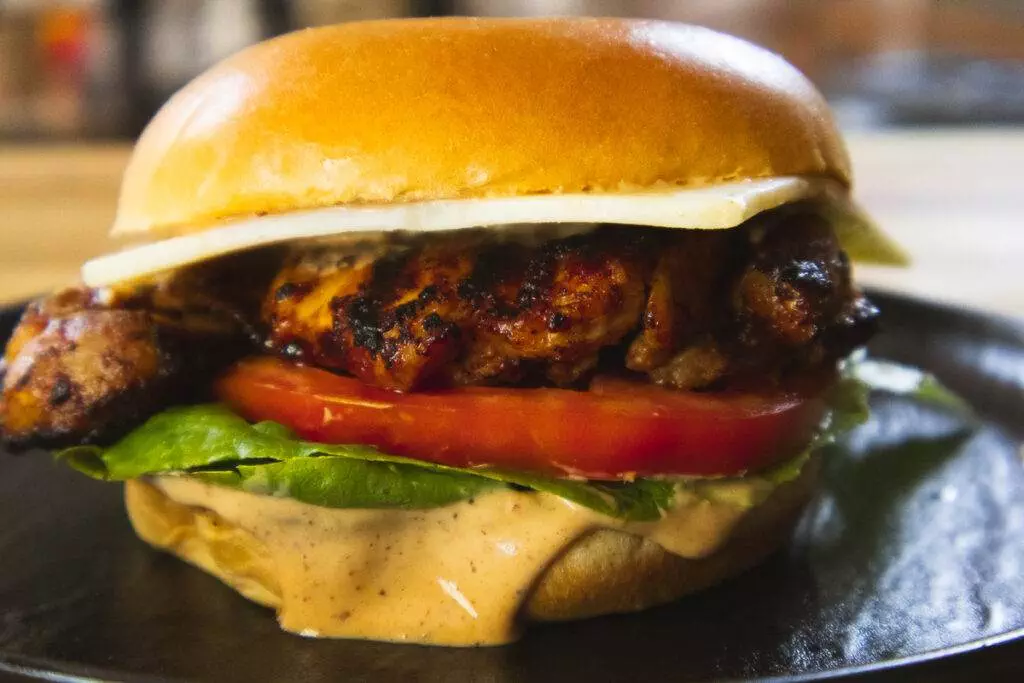 Close-up of a juicy grilled chicken sandwich with fresh lettuce, tomato, and creamy sauce on a toasted brioche bun.