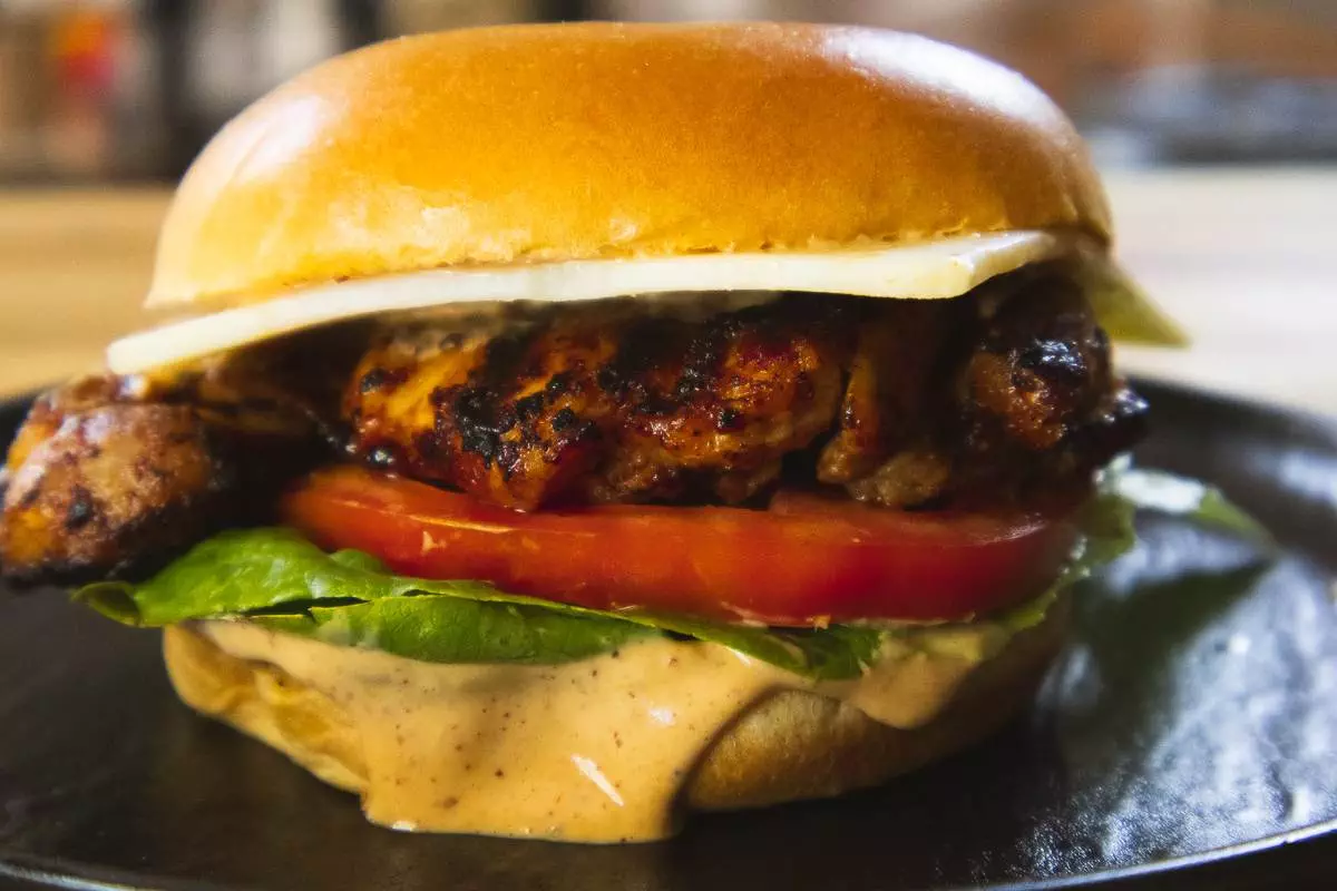 A close up of a juicy, grilled chipote chicken burger with lettuce, tomato, sauce and cheese