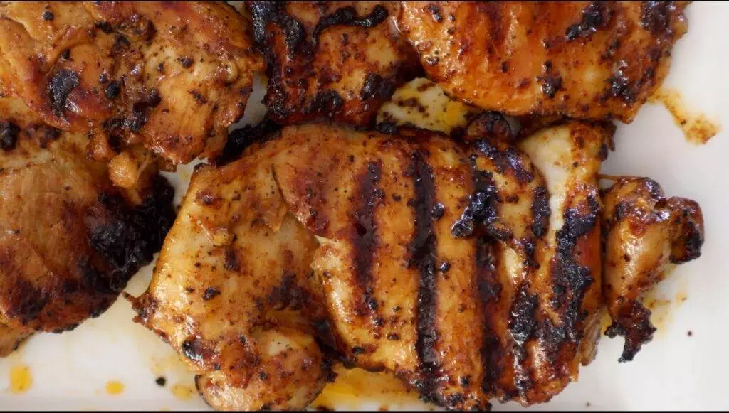 Grilled chicken thighs with savory char marks on a white plate, perfect for a delicious barbecue meal.