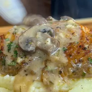 Delicious mushroom gravy sauce chicken over mashed potatoes, garnished with herbs. Perfect comfort food dish.