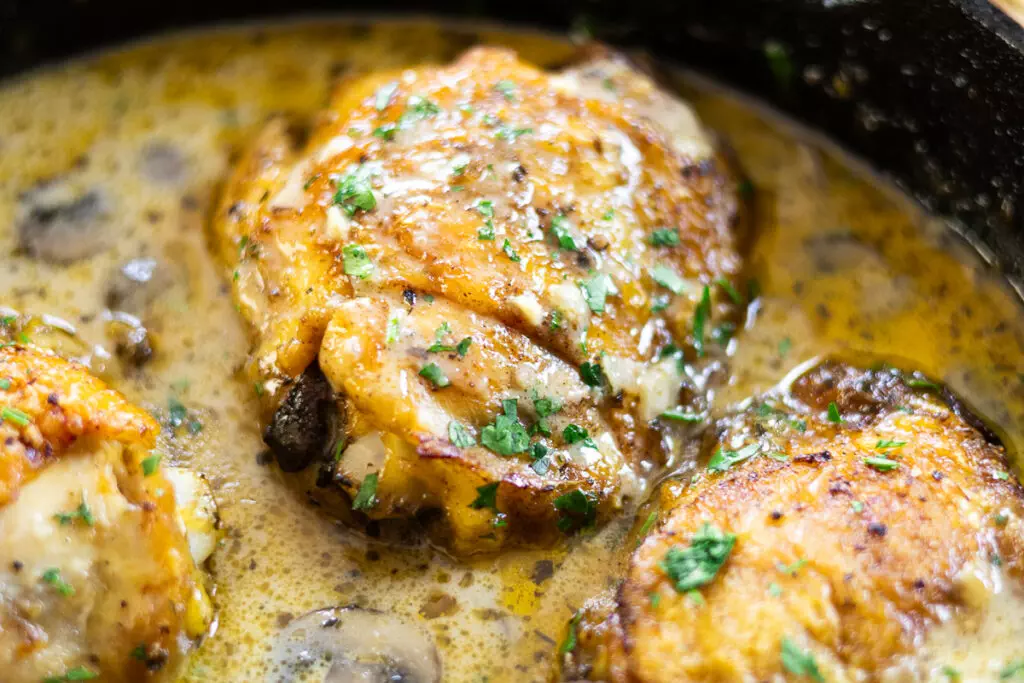 Creamy garlic chicken thighs with herbs in a skillet, perfect for a savory home-cooked meal.