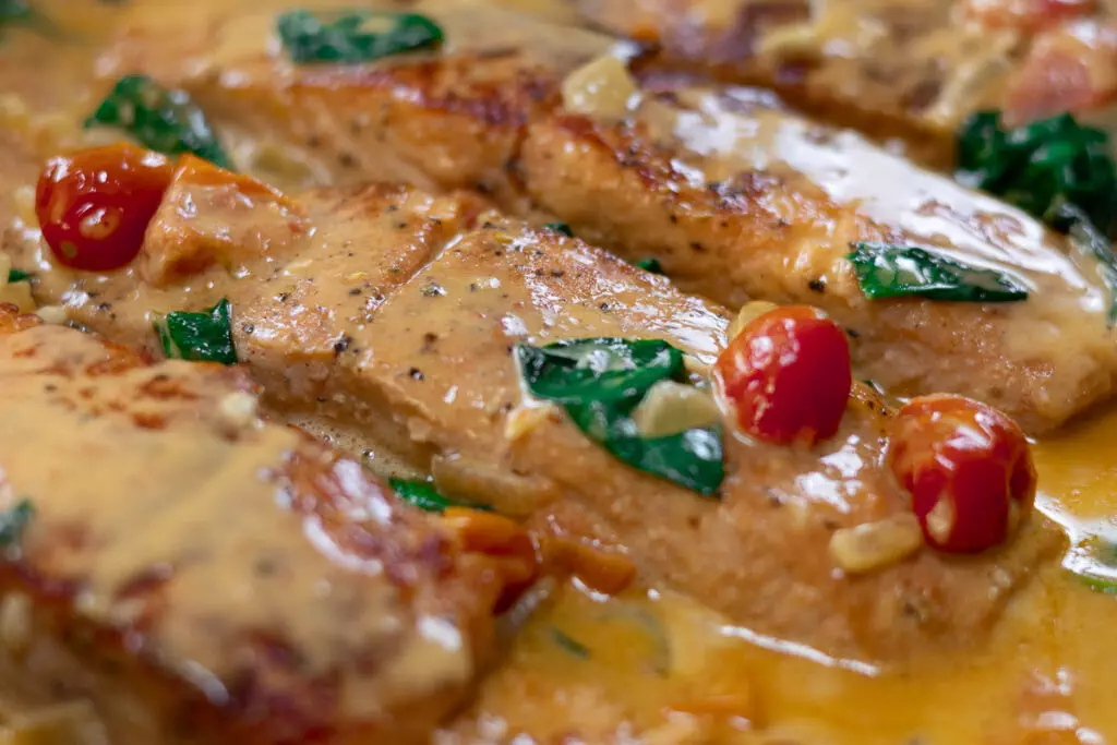 Creamy tuscan salmon with cherry tomatoes and spinach in rich sauce. Perfect for a delicious dinner idea.