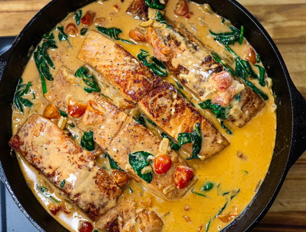 Pan-seared tuscan salmon in a creamy tomato and spinach sauce, cooked to perfection in a black skillet.