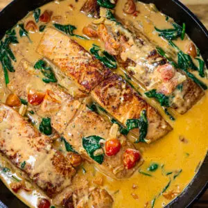 Pan-seared salmon in a creamy tomato and spinach sauce, cooked to perfection in a black skillet.