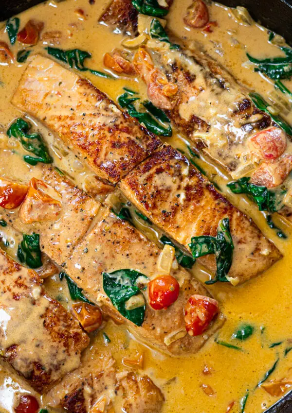 Pan-seared salmon in a creamy tomato and spinach sauce, cooked to perfection in a black skillet.